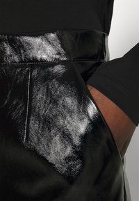 Svart fusk läderkjol med en glänsande yta, med en bred midjeband och en sidoficka. Närbild visar texturen och den släta designen.