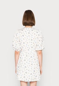 Blumenkleid mit Puffärmeln, weißem Hintergrund, kleinen blauen und gelben Blumenmustern, tailliertem Bund und knielanger Länge.