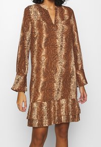 Ruskea ja beige kuviollinen mekko, jossa on V-pääntie, pitkät hihat ja röyhelöhelma, valmistettu kevyestä kankaasta.