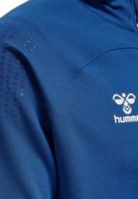 Niebieska tkanina sportowa z logo kolibra i nazwą marki „hummel” nadrukowaną na biało na obszarze klatki piersiowej.