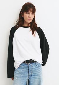 Langærmet t-shirt i bomuld med hvid krop og sorte raglanærmer. Kombineret med lyseblå, distressed jeans med malingsplamager.