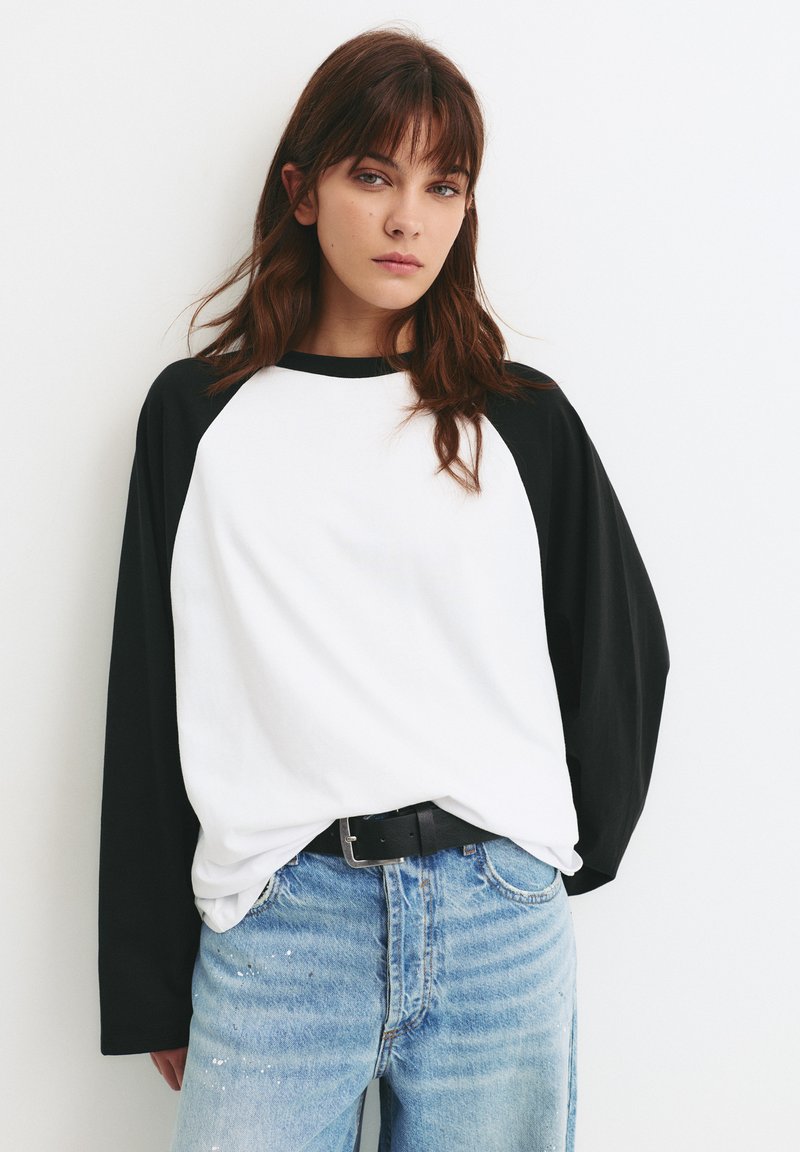 Langærmet t-shirt i bomuld med hvid krop og sorte raglanærmer. Kombineret med lyseblå, distressed jeans med malingsplamager.