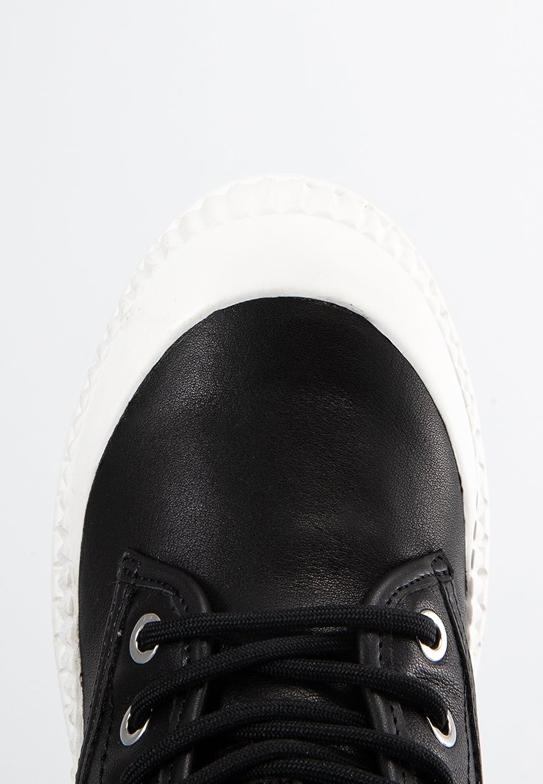 Baskets en cuir noir avec un bout arrondi, semelle en caoutchouc blanche et lacets noirs. Présentent des œillets métalliques et une texture lisse.