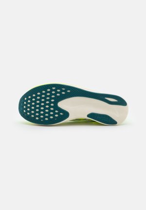 Semelle de chaussure de course avec motifs en caoutchouc blanc et vert foncé sur fond gris clair.