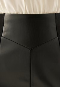 Černá kožená sukně s hladkou texturou a geometrickými švy na pásku. Ozdobená kontrastní látkou po stranách.