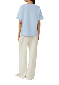 Lichtblauw oversized t-shirt van zacht katoen, met korte mouwen en een ronde halslijn, gecombineerd met losse, crème-kleurige broeken.