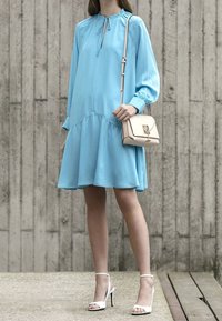 Ljusblå, långärmad klänning med rynkad midja och flödande kjol. Matchad med vita högklackade sandaler och en liten handväska i crème.