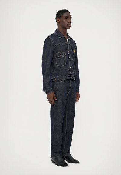 Mørkeblå denimjakke og matchende bukser, der har to forlommer, knaplukning og diskrete syninger.