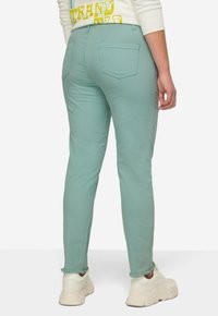 Pantalones ajustados de color verde menta con bolsillos traseros, pierna cónica y dobladillos enrollados. Combinar con zapatillas blancas completa el look.
