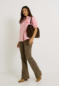 Camisa de botones a rayas rojas y blancas con un bolsillo en el pecho, combinada con pantalones de campana marrón con estampado de leopardo y un bolso de hombro marrón oscuro.