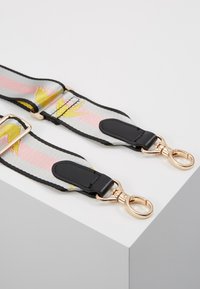 Taška s květinovým vzorem má stříbrno-šedý základ se lila pásky, černé kožené akcenty a kovové doplňky ve zlaté barvě.