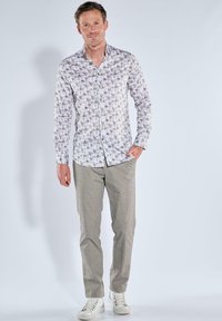 Weißes Hemd mit Knopfleiste und floralem Muster in Grün und Lila, kombiniert mit hellgrauen Hosen und weißen Turnschuhen. Glatter Stoff, lockere Passform.