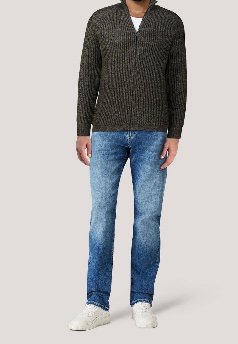 Mörkgrön, räfflad zip-up-tröja med hög krage, bärs över en vit skjorta, tillsammans med ljusblå jeans och vita sneakers.