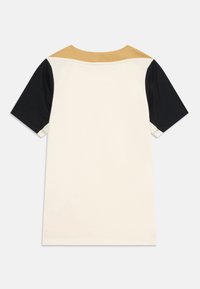 T-shirt s kratkimi rokavi v kremni barvi, z črnimi in svetlo rjavimi poudarki na ramenih. Gladka tkanina, sproščen kroj, okrogla vrhnja obleka.