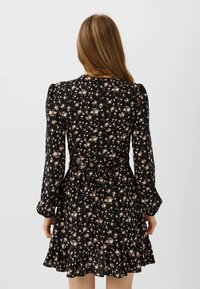 Schwarzes Kleid mit langen Ärmeln, florales Muster in Rosa und Weiß. Verfügt über eine taillierte Taille und einen gerafften Saum. Leichtes Material mit klassischem Design.