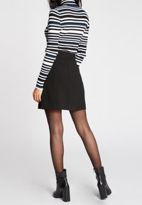 Zwarte rok met een aansluitend ontwerp, gecombineerd met een zwart-wit gestreepte turtleneck. Gekenmerkt door doorschijnende panty's en chunky zwarte laarzen met hoge hakken.