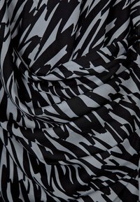 Schwarz-grau gemusteter Stoff mit welliger Textur, der scharfe, abstrakte Linien zeigt und einen dynamischen Kontrast über die Fläche erzeugt.