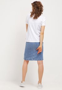 Vit bomull t-shirt och blå denimkjol, knälång, med rak skärning och fransad fåll. Kombinerad med vita sneakers.