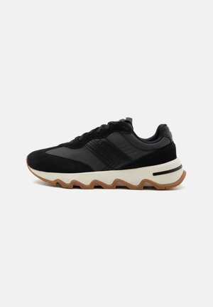 Sort lav sneakers med snørelukning, hvid bølget mellemsål, tekstureret gummiydersål og polstret krave mod en hvid baggrund.
