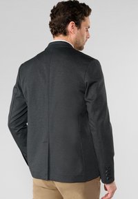 Blazer gris foncé en tissu texturé, avec une fente simple au dos et des poignets boutonnés. Coupe ajustée mise en valeur par la vue arrière.