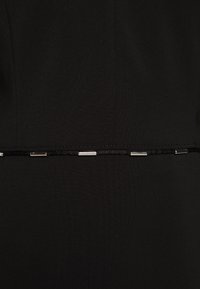 Tissu noir avec un cordon noir horizontal parcouru de petits tubes métalliques argentés espacé régulièrement au centre.