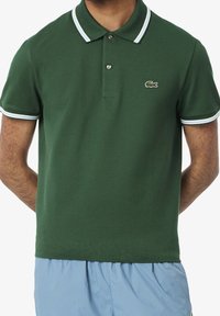 Zielona koszulka polo z teksturowanej tkaniny, z dwoma guzikami, kołnierzykiem i mankietami w białe i niebieskie paski oraz detalem logo.
