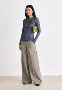 Maglietta a maniche lunghe, blu navy con pois verdi, abbinata a pantaloni larghi grigio chiaro. L'outfit è completato da una piccola borsa verde.