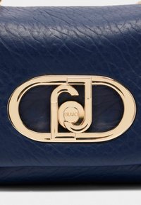 Borsa a tracolla in pelle blu navy con un prominente fermaglio in metallo dorato. Il materiale presenta una finitura testurizzata congrandi venature visibili.