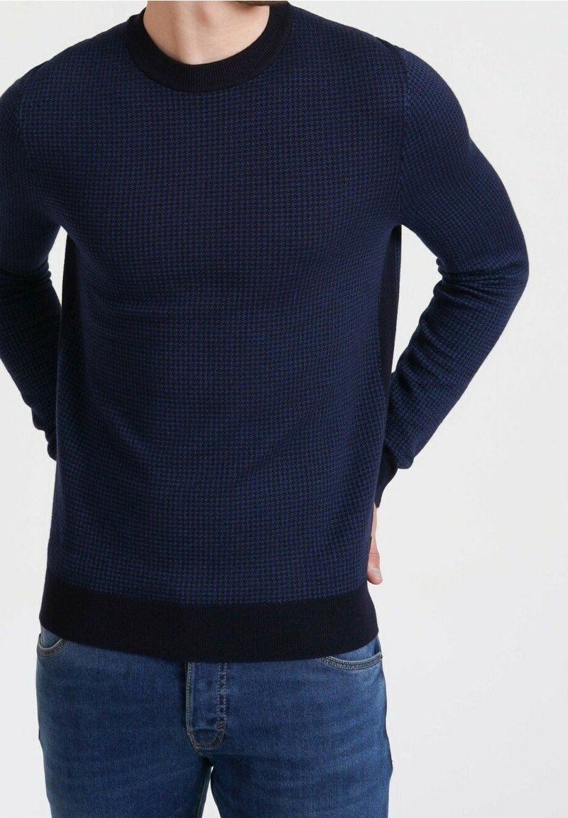Pull bleu marine avec motif texturé, encolure ronde, poignets et ourlet en côte. Associé à un jean en denim bleu clair.