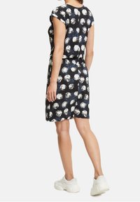 Robe noire présentant un motif de formes circulaires blanches, manches courtes, taille élastique, et longueur au-dessus des genoux. Portée avec des baskets blanches.