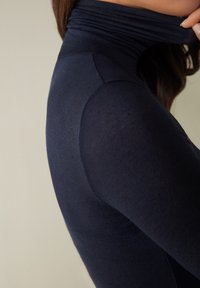 Námořnický modrý rolák s přiléhavým střihem, hladkou texturou a nařaseným materiálem u krku. Viditelné detaily bočních švů.