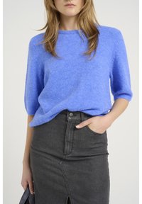 Pull bleu en maille douce avec un col rond et des manches courtes, associé à une jupe en denim foncé taille haute avec une fente à l'avant.