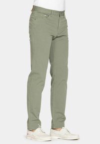 Chinos in cotone verde chiaro, slim fit, con quattro tasche e chiusura a bottone in metallo. Indossati con scarpe beige slip-on.