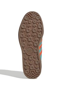 Podešev tenisky Adidas s kruhovým vzorem gripu, hnědý gumový materiál, s zelenými a oranžovými akcenty na horní straně. Logo ve středu.