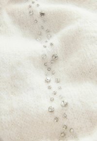 Biele pletené tkaniny s jemnou textúrou, s radom čírych rhinestones rôznych veľkostí pozdĺž povrchu.