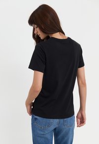 Black short-sleeve t-shirt made from cotton, featuring a crew neckline and a fitted cut. Worn with blue denim jeans.
