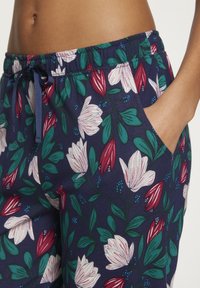 Pantalones de salón florales con un fondo azul marino decorado con flores blancas y rojas y hojas verdes, equipados con bolsillos laterales y una cintura con cordón.