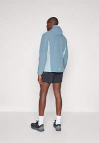 Hoodie in Hellblau mit dunkleren blauen Akzenten, aus leichtem Material gefertigt. Verfügt über lange Ärmel und einen lässigen Schnitt, kombiniert mit schwarzen Shorts.