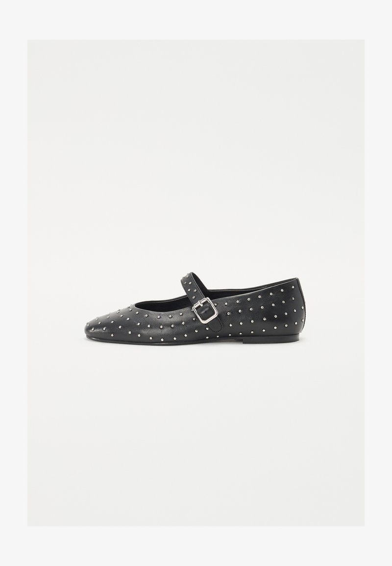 Black leather flat shoe with a pointed toe, adorned with silver studs, featuring a decorative strap with a buckle. Smooth texture, low heel.