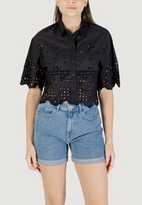Maglietta nera corta con motivo floreale a perforazione, maniche corte e chiusura a bottoni; abbinata a pantaloni corti in denim azzurro a vita alta.