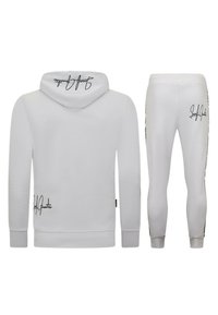 Witte hoodie en bijpassende broekset, voorzien van zwarte geschreven logo's op beide items en een zachte stoftextuur. Mouwen en broeken zijn slim fit.