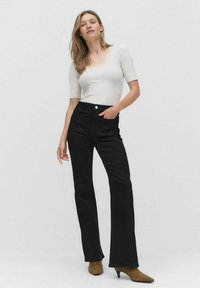 Sorte flared jeans med høj talje og forlommer, parret med en hvid top med rund udringning og blonderkant. Brune hæle støvler.