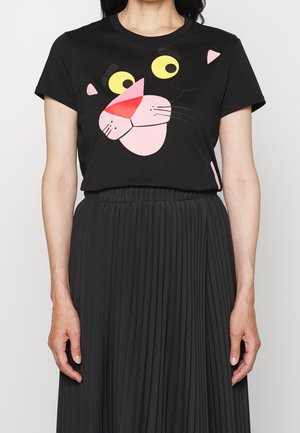 Person trägt ein schwarzes T-Shirt mit einem großen bunten Cartoon-Katzengesicht und einen hoch taillierten schwarzen Faltenrock.