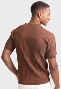 Braun kurzärmliges Strick-Polohemd mit vertikaler Ripptextur, flachem Kragen und tailliertem Schnitt. Besteht aus einem glatten, leichten Stoff.