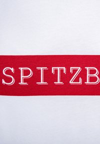 Weißes T-Shirt aus Stoff mit einem auffälligen roten horizontalen Streifen, auf dem das Wort "SPITZ" in weißer Stickerei hervorgehoben ist, was ein sauberes, modernes Design unterstreicht.