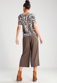 Haut à manches courtes imprimé peau de serpent, associé à un pantalon large taupe. Des bottines marron à talon bloc complètent la tenue.