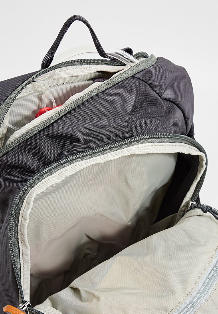 Mochila negra de nailon con acentos grises, que cuenta con dos compartimentos con cremallera. El interior está forrado con una tela más clara, mostrando un amplio espacio de almacenamiento.