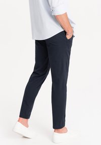 Pantaloni di cotone navy con vestibilità slim, dotati di tasche laterali e una texture liscia, abbinati a scarpe bianche slip-on.