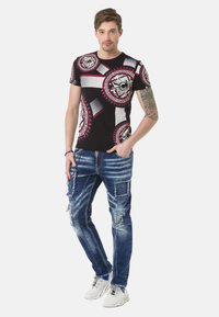 Schwarzes T-Shirt mit kräftigem roten und weißen kreisförmigen Grafikdesign, kombiniert mit abgenutzten blauen Jeans mit Patches und ausgefransten Kanten.