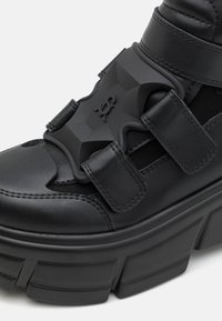 Svarta läderskor med plattform och kraftig sula, med kardborreband och en texturerad gummidetalj på ovandelen för extra detalj.
